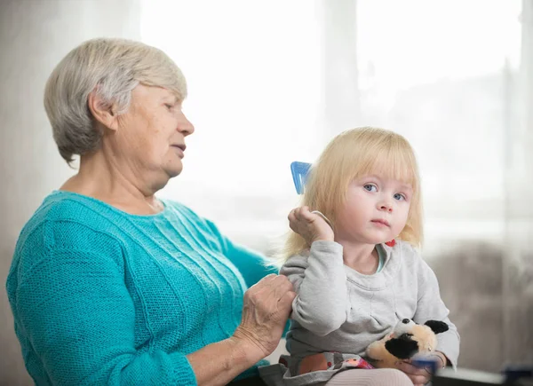 Бабушка расчесывает светлые волосы своей внучке — стоковое фото