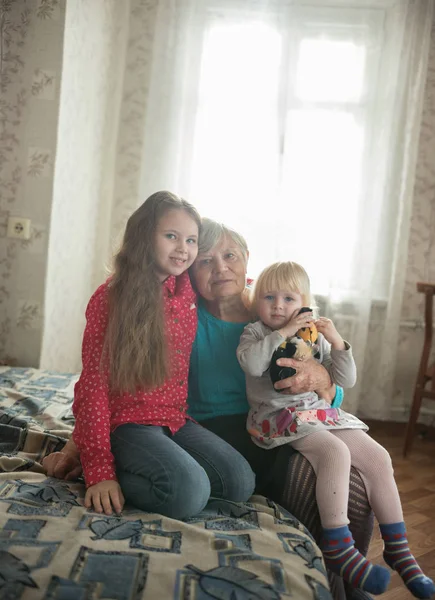 Lycklig familj sitter på sängen. Två flickor och mormor — Stockfoto