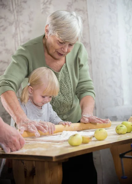 Бабушка делает пирожки с маленькой девочкой. Роллинг тесто — стоковое фото