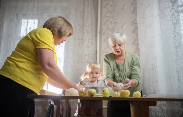 Dos ancianas haciendo tartas de manzana con una niña en casa — Foto de Stock
