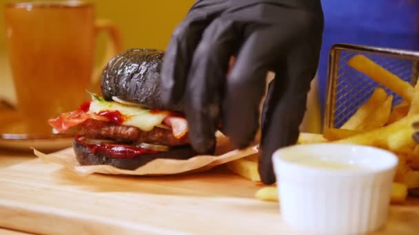 Un burger negru cu bacon și sos bbq pe un birou din lemn servit cu cartofi prăjiți — Videoclip de stoc