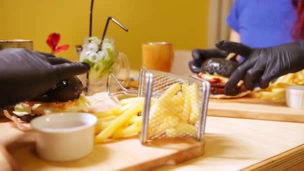 Two people in black gloves taking black burgers from a table — Stock Video