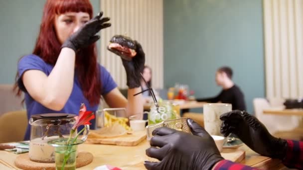 Siyah bir kafede oturan ve yemek iki insanlar hamburger — Stok video