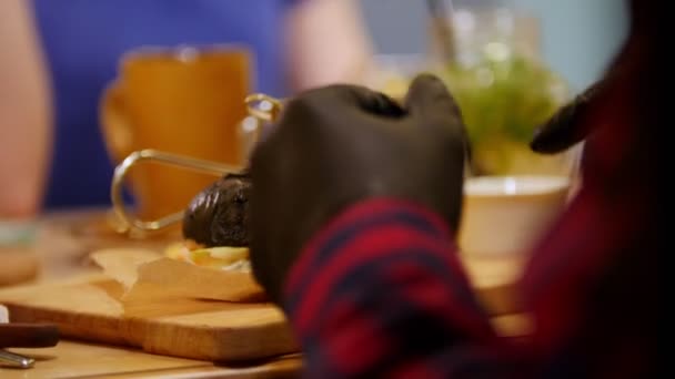 Два человека сидят в кафе у стола и едят черные бургеры — стоковое видео