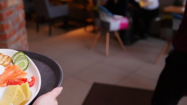 Ein Paar, das in einem Café am Tisch sitzt. Kellner kommt zu ihnen durch das Café und bringt das Gericht — Stockvideo