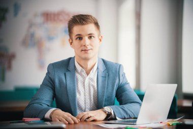 Genç işadamı ofiste dizüstü bilgisayarla çalışıyor.