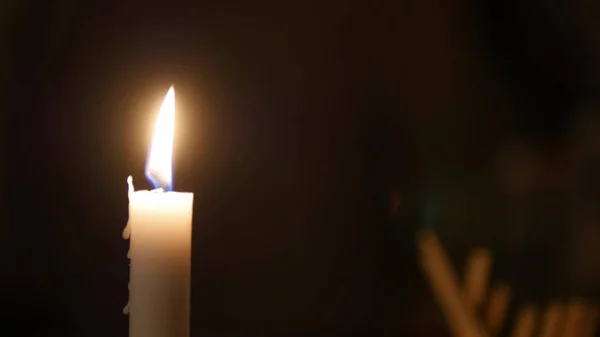 Крупним планом полум'я свічки на чорному тлі, хтось рухається за свічкою — стокове фото