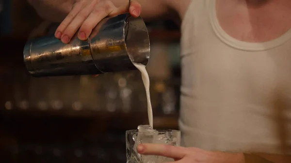 Jovem barman profissional derramando bebida creme branco no copo cheio de gelo — Fotografia de Stock