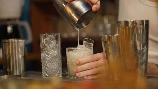 Jovem barman profissional derramando bebida branca no copo cheio de gelo — Fotografia de Stock