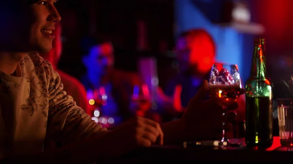Бар з неоновим освітленням. Чоловік сидить за столом і п'є пиво — стокове фото