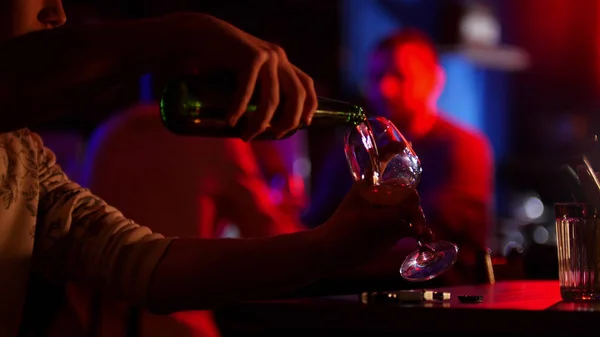 Bar com iluminação de néon. Um homem derramando cerveja de uma garrafa em um copo — Fotografia de Stock