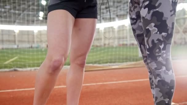 Dos mujeres hermosas jóvenes escuchando música usando auriculares en la sala de deportes después del entrenamiento — Vídeo de stock