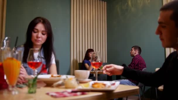 Een jong koppel zitten bij de tafel in een café. Eten en drinken — Stockvideo