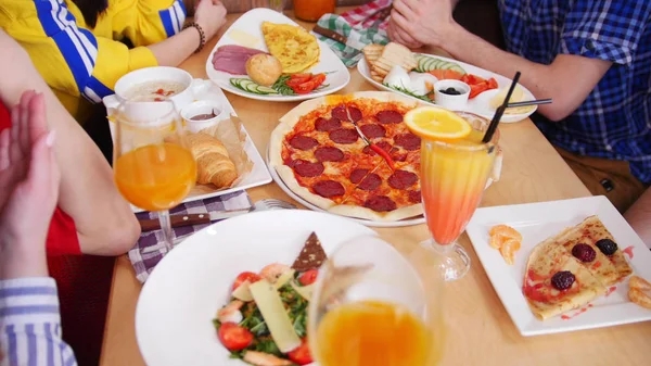 Группа друзей, сидящих в кафе. Стол с едой и пиццей пепперони в центре — стоковое фото