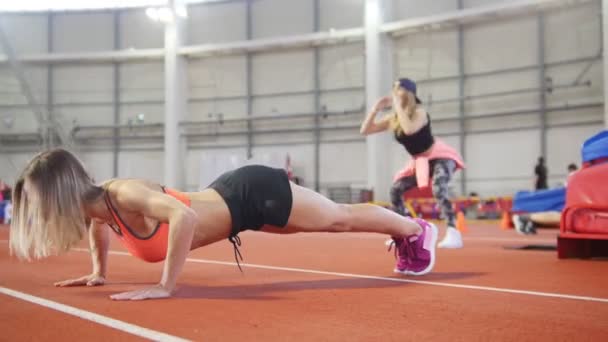 Athletische Frau in Sportkleidung beim Liegestütz. eine weitere Frau wärmt sich auf einem Hintergrund auf — Stockvideo