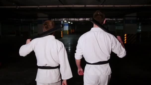 彼らの肩に訓練剣を保持している駐車場の上を歩く着物姿の 2 人の男性 — ストック動画