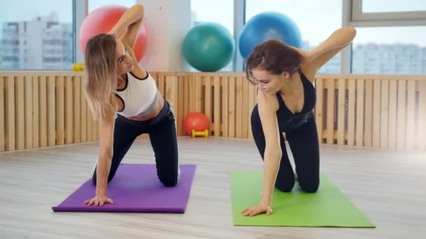 Jovens mulheres fazendo ioga no estúdio. O treinador mostra um novo exercício e a jovem repete — Vídeo de Stock