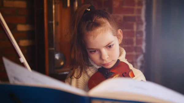 Uma menina concentrada tocando violino por notas — Fotografia de Stock