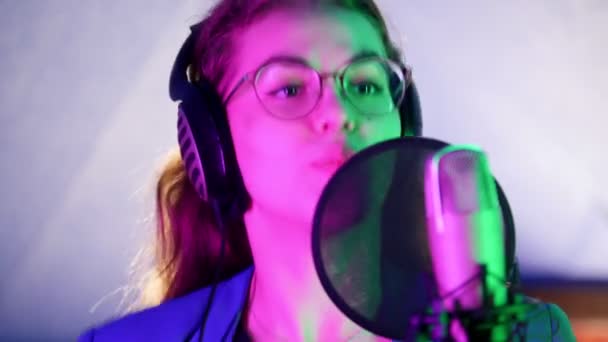 Eine junge lächelnde Frau mit Kopfhörern, die im Studio singt. Neonbeleuchtung — Stockvideo