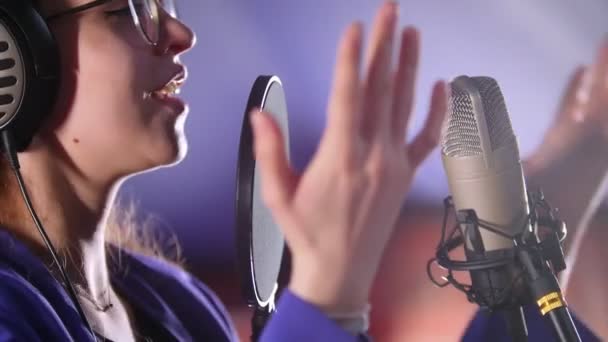 Une jeune femme à lunettes enregistrant une chanson en studio — Video