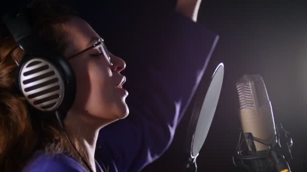 Seorang wanita muda yang emosional berkacamata merekam sebuah lagu di studio — Stok Video