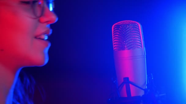 Молодая эмоциональная женщина в наушниках поет в студии. Неоновое освещение — стоковое видео