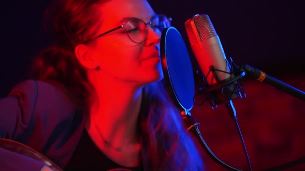 Eine junge Frau mit Brille, die Gitarre spielt und in Neonlicht singt — Stockvideo