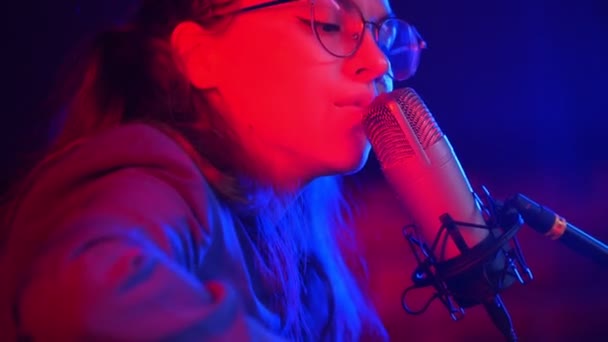 Eine junge Frau geht durch die Saiten der Gitarre und singt ein Lied in Neonlicht — Stockvideo