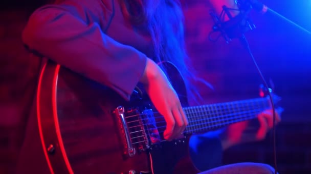 Una joven pasa por las cuerdas de la guitarra y canta una canción romántica con iluminación de neón — Vídeos de Stock