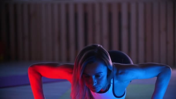 Trener fitness młoda kobieta robi push up w studio w neon oświetlenie — Wideo stockowe