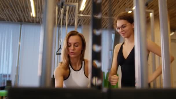 Junge Frauen beim Fitnesstraining im Fitnessstudio. eine Frau macht Kraftübungen. eine andere Frau beobachtet sie und versucht es — Stockvideo