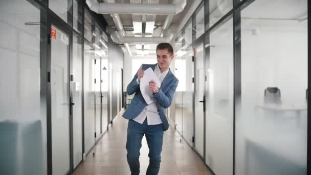 Un empresario excitado bailando en el pasillo de la oficina, señalando a sus colegas y sonriendo . — Vídeos de Stock