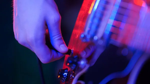 Молодий музикант грає на гітарі в неоновому освітленні. Увімкнення вилки — стокове фото