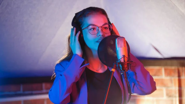 Молода жінка в окулярах співає в неоновому освітленні в студії — стокове фото