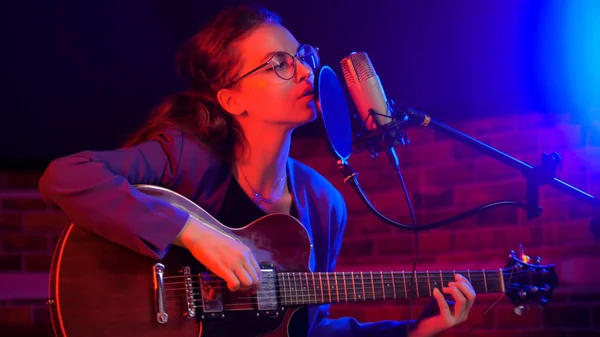 Uma jovem mulher tocando guitarra e cantando em iluminação de néon — Fotografia de Stock