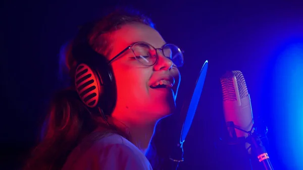 A young smiling emotional woman in glasses singing in neon lighting in the studio — Stock Photo, Image