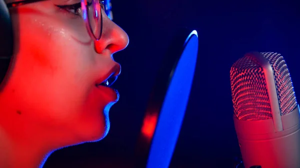 Молодая женщина в очках поет в неоновом свете у микрофона — стоковое фото