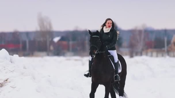 Una joven con el pelo largo y lápiz labial rojo montando a caballo en un pueblo — Vídeos de Stock