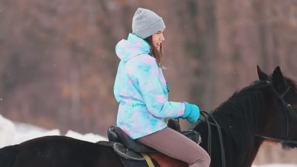 Зимовий час, снігопад. Молода жінка верхи на коні в селі — стокове відео