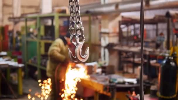 Construction plant. A big industrial lifting chain with a hook on the end. A man welding on the background — Stock Video