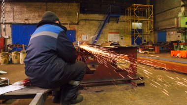 Taşlama tezgahı ile çalışan bir adam. Yangın parıldıyor