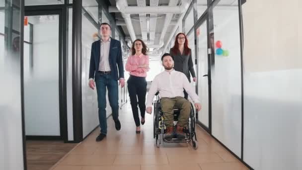 Um empresário de sucesso a caminhar pelo corredor no centro de escritórios. Um homem em uma cadeira de rodas vai primeiro — Vídeo de Stock