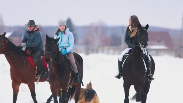 Tres mujeres montando a caballo en un pueblo con un perro corriendo cerca de ellas — Vídeos de Stock