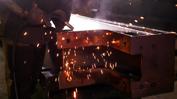 Um homem na fábrica de construção usando uma máquina de solda. Brilhantes caindo no chão — Fotografia de Stock