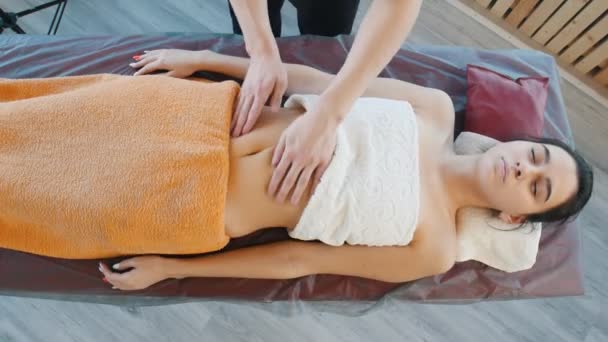 A masseur preparing a young woman for the relaxing stomach massage with stroking motions — Stock Video