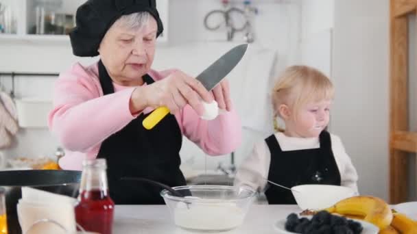 Сімейне виготовлення млинців. Стара жінка додає яйця в тісто — стокове відео