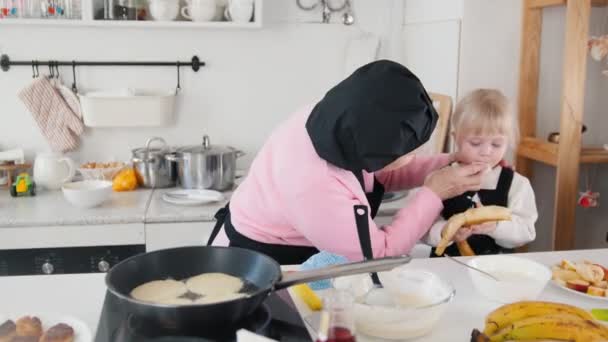 Οικογένεια κάνει τηγανίτες. Μια ηλικιωμένη γυναίκα που τον καθαρισμό του στόματος κοριτσάκια από τη ζύμη — Αρχείο Βίντεο