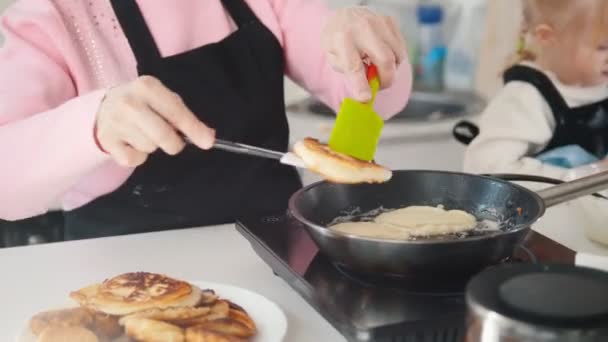 Een oude vrouw pannenkoeken maken in de keuken. De pannenkoek op de plaat te zetten — Stockvideo