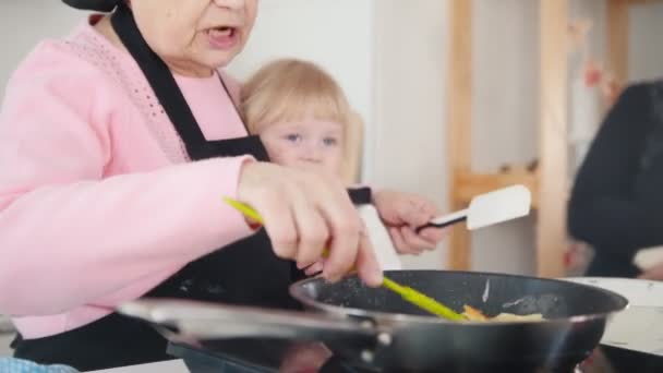 늙은 여자 밝은 부엌에서 팬케이크를 만들고 어린 소녀 포옹 — 비디오