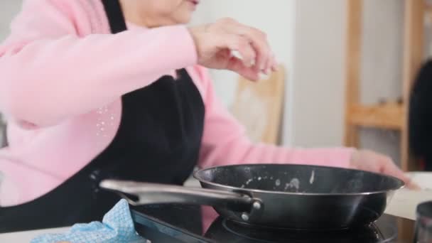 Eine alte Frau macht Pfannkuchen aus den Teigresten — Stockvideo